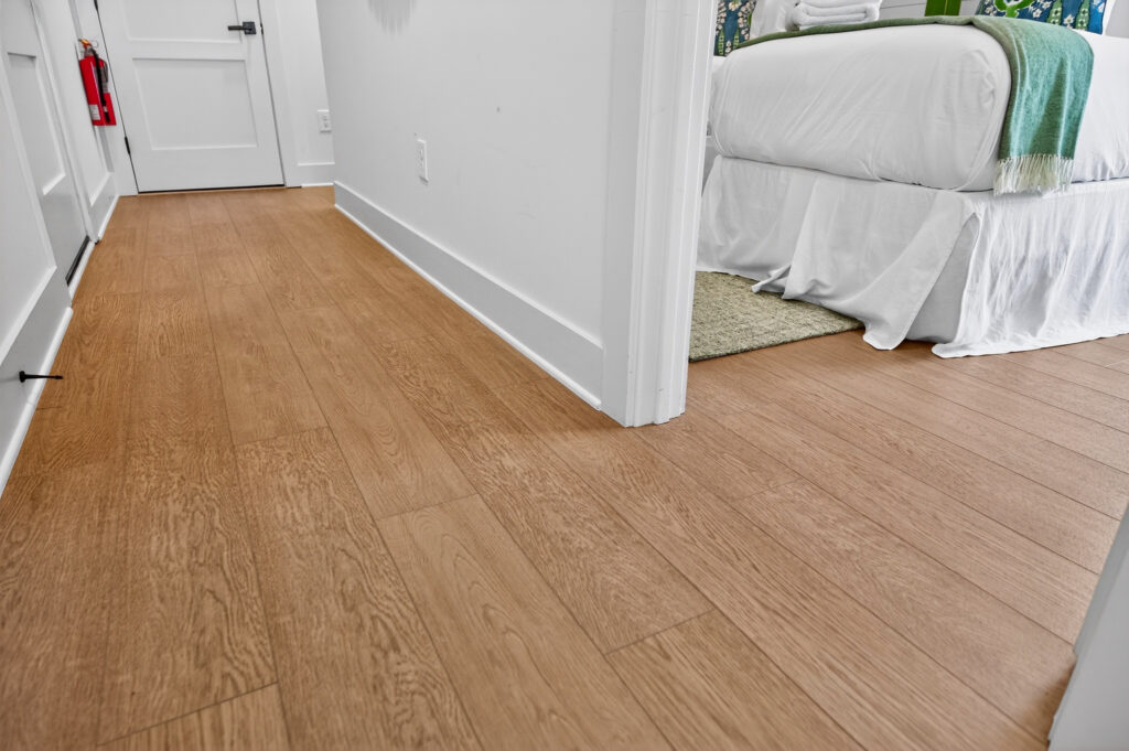 Close-up of light wood-look plank flooring and white baseboard at Winyah Bay Club, installed by J&S Flooring