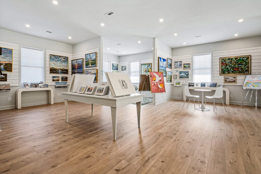 Gray Man Gallery with white display table, framed art and light wood plank flooring
