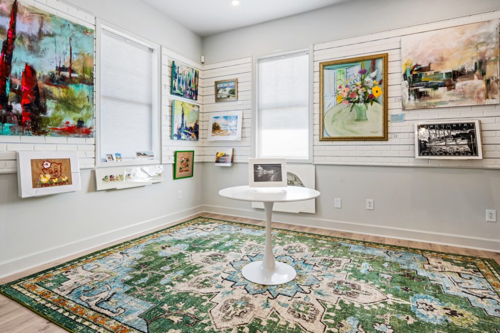 Gray Man Gallery with framed paintings, round white table and green area rug