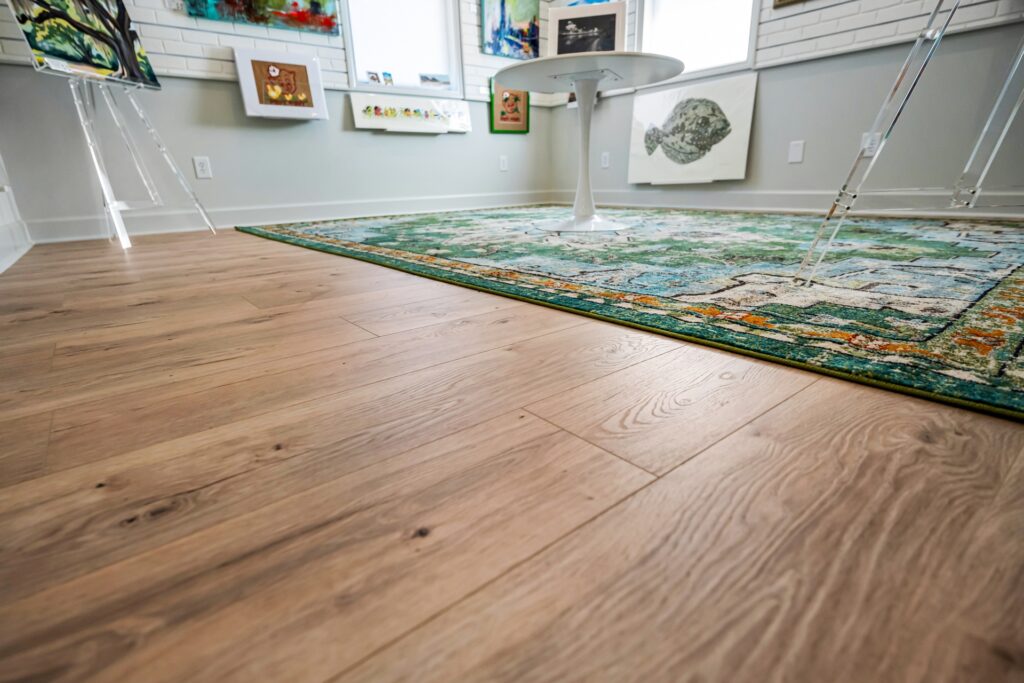 Wide-plank light wood flooring with green patterned area rug at Gray Man Gallery