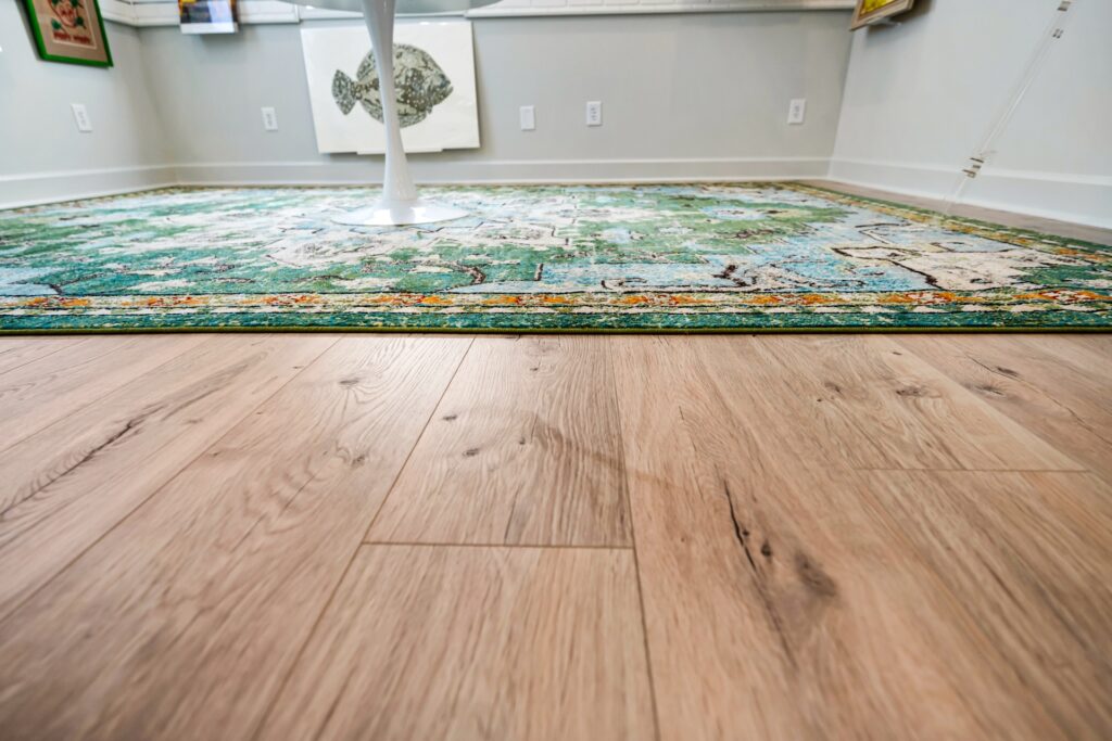 Close-up of light wide-plank wood flooring and green patterned rug at Gray Man Gallery