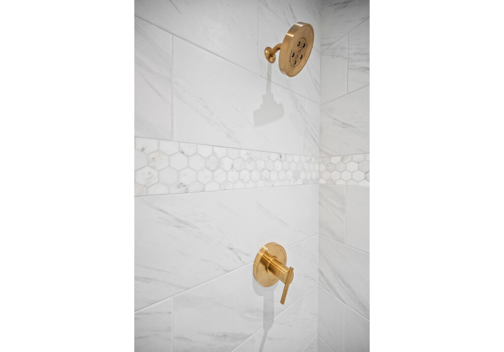 Collins Meadows shower with marble-look tile, hexagon accent and brass shower fixture