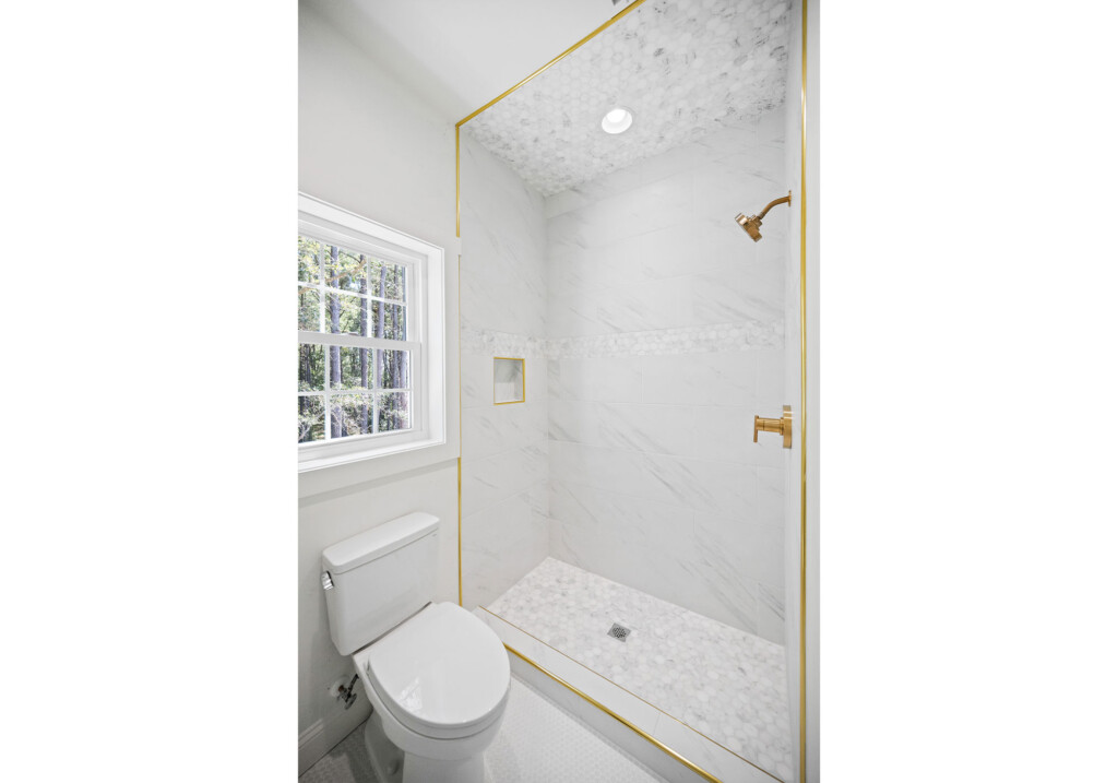 Collins Meadows bathroom shower with gold trim, marble-look tile and window