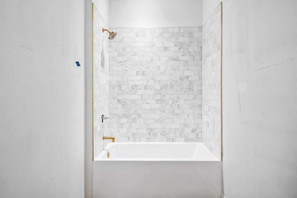 Collins Meadows bathtub with marble-look tile surround and brass fixtures