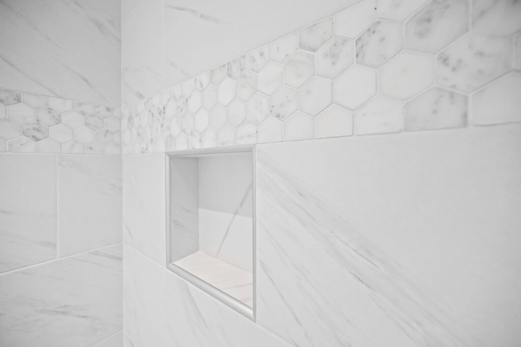 Collins Meadows shower with marble-look tile and hexagon accent band, tile by J&S Flooring