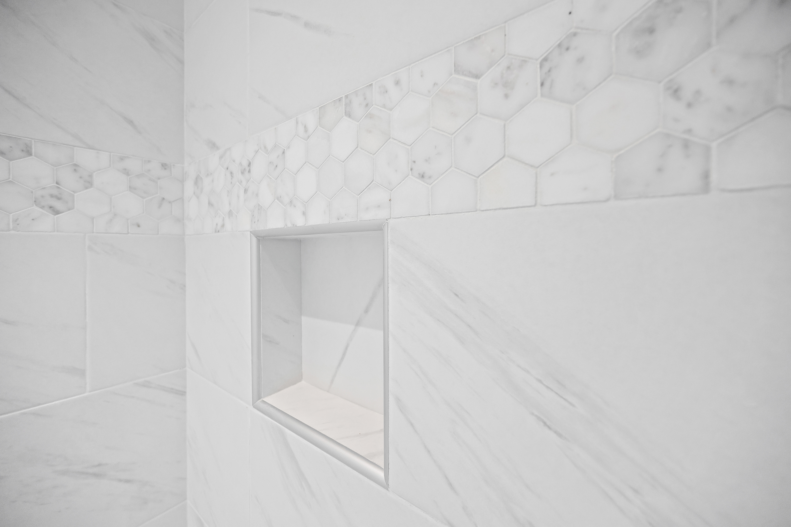 Collins Meadows shower with marble-look tile and hexagon accent band, tile by J&S Flooring