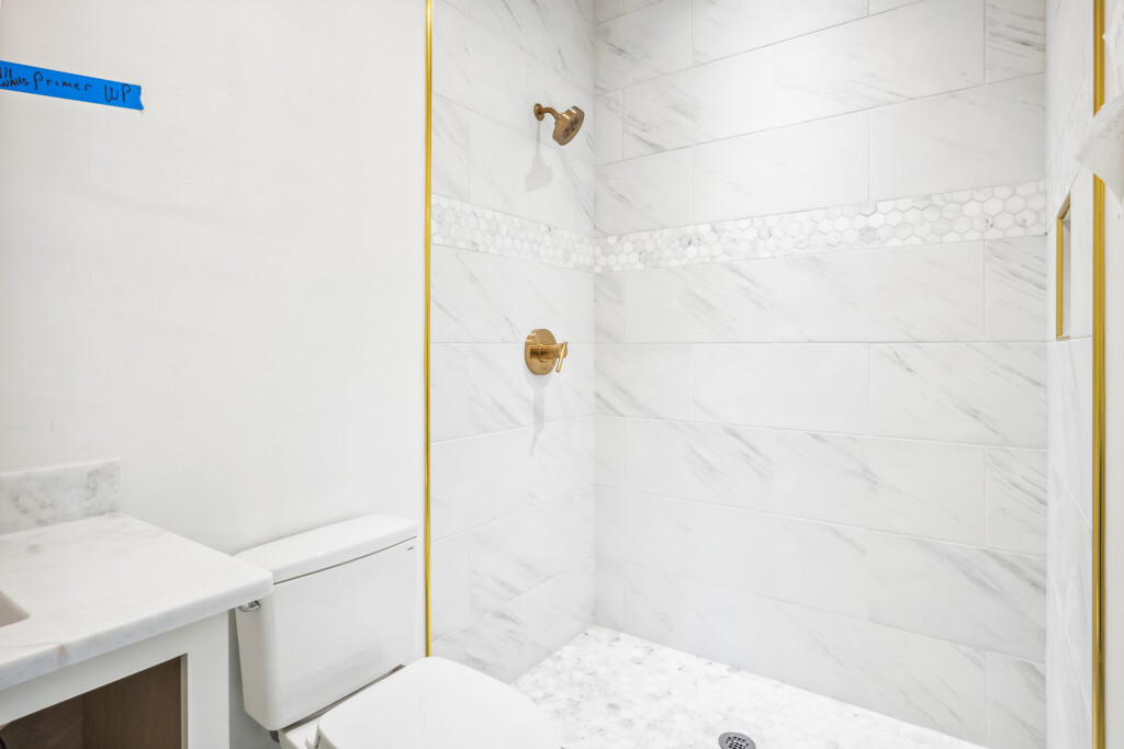 Collins Meadows shower with gold trim and brass fixture on marble-look tile