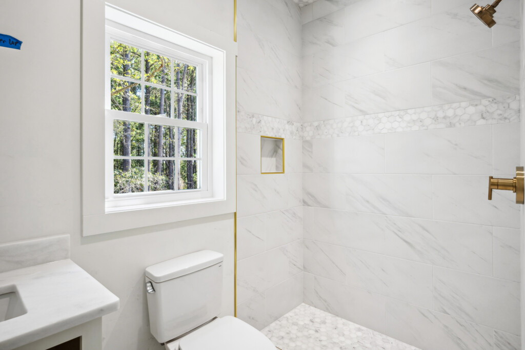 Collins Meadows shower with large-format marble-look tile and gold trim, tile by J&S Flooring in Georgetown, SC