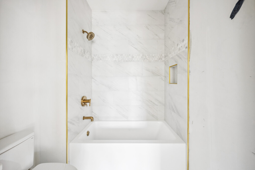 Collins Meadows tub and shower with marble-look tile and brass tub spout