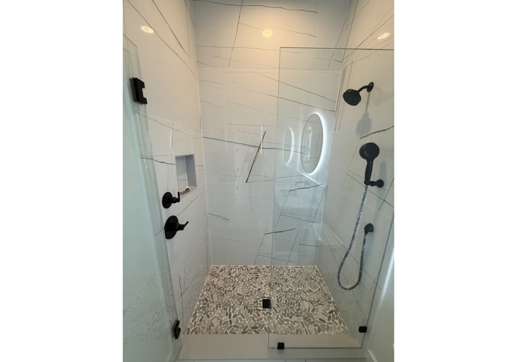 Woodward Project walk-in shower with tile niche, handheld shower and pebble tile floor