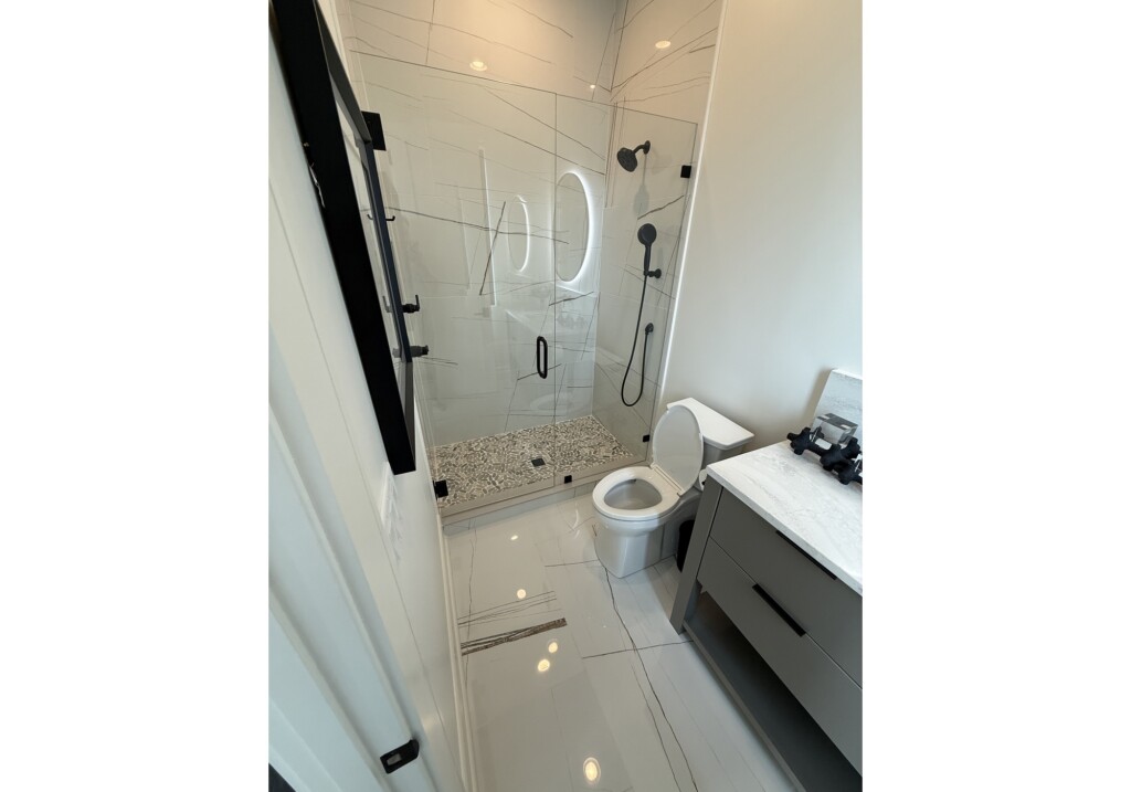 Woodward Project bathroom with glass shower, pebble tile floor and navy vanity