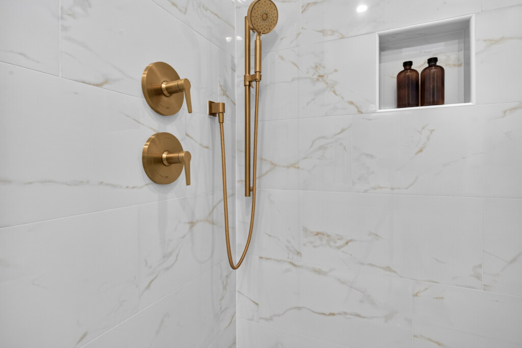 Shower wall with large-format marble-look porcelain tile and brass fixtures