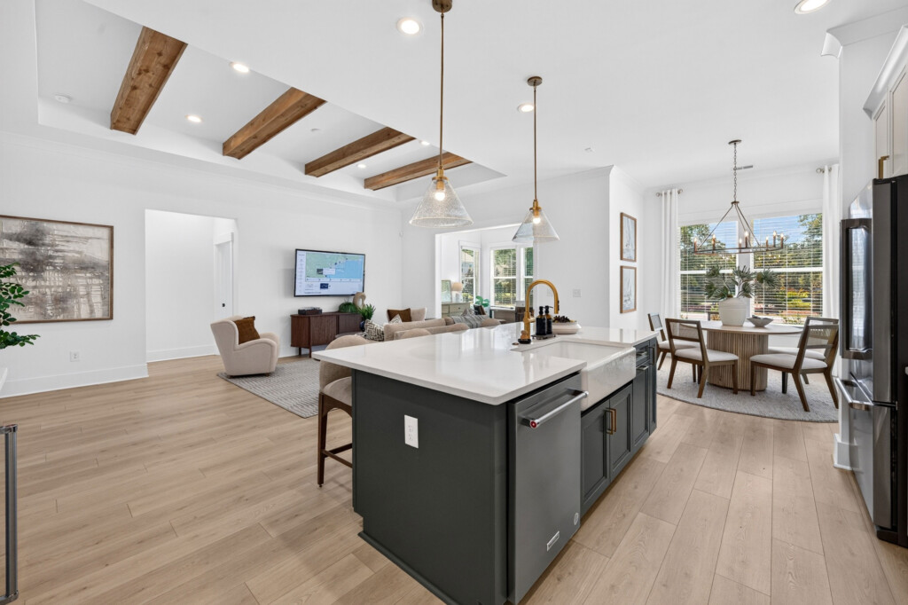 Open kitchen and living area with a dark island, wood beams, and light plank flooring