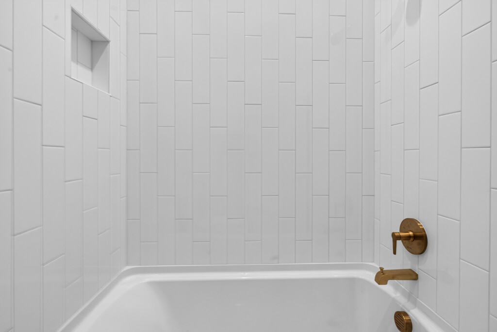 Bathtub with vertical white tile surround and brass fixtures
