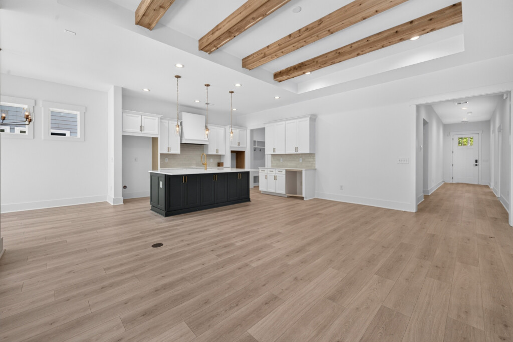 Great room and kitchen with exposed beams and light wood-look plank flooring