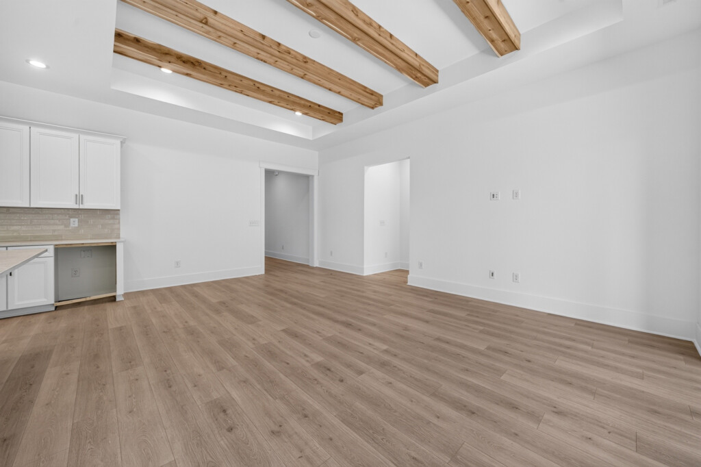 Unfurnished living area with wood beams and light plank flooring