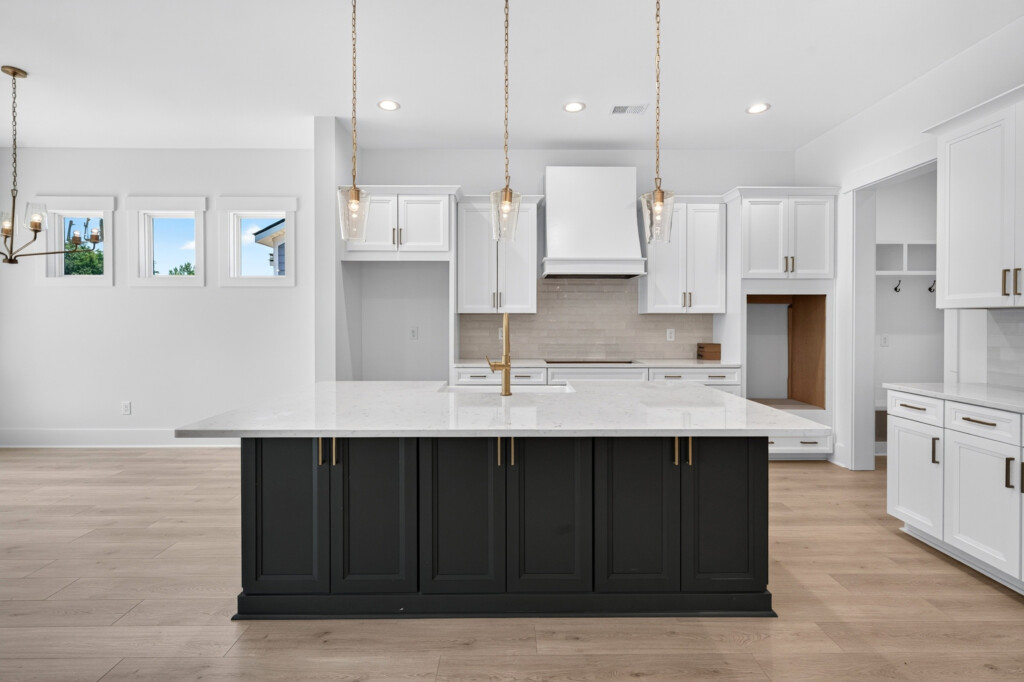 Kitchen with dark island, white cabinets, and light wood-look plank flooring