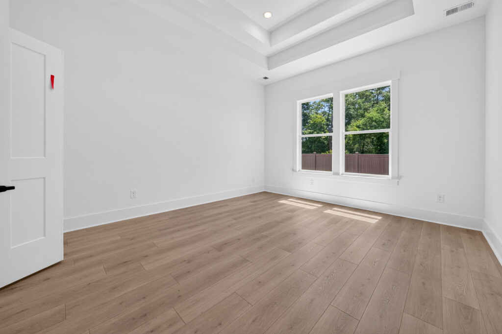 Empty bedroom with tray ceiling and light wood-look plank flooring