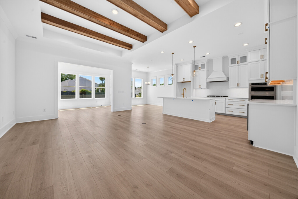 Open great room and white kitchen with exposed beams and plank flooring