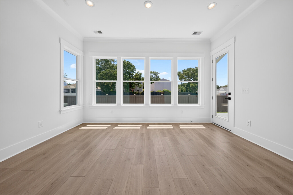 Empty living room with a bank of windows and light plank flooring