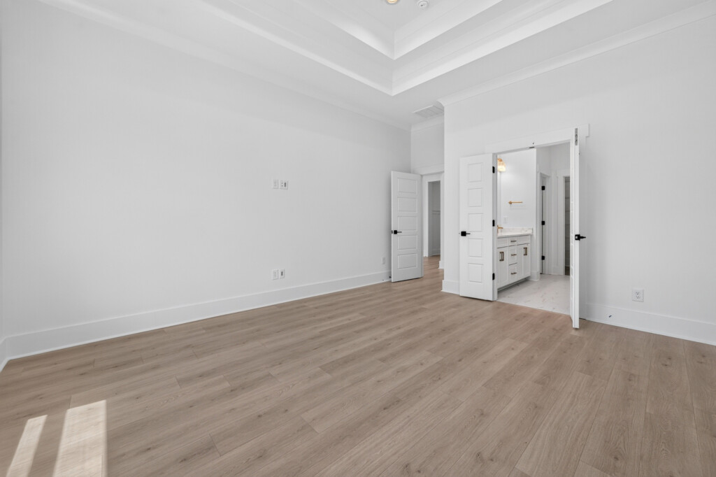 Primary bedroom with light plank flooring and view into the bathroom