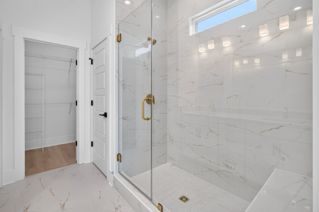Glass shower with marble-look tile next to walk-in closet