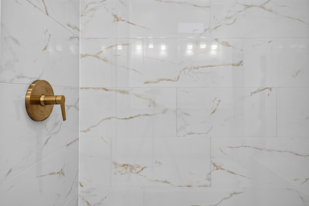 Close-up of marble-look porcelain shower tile with brass valve